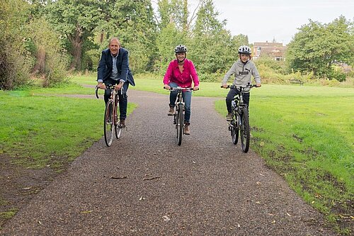 two adults and a teenager cycling on a cycle path in a field