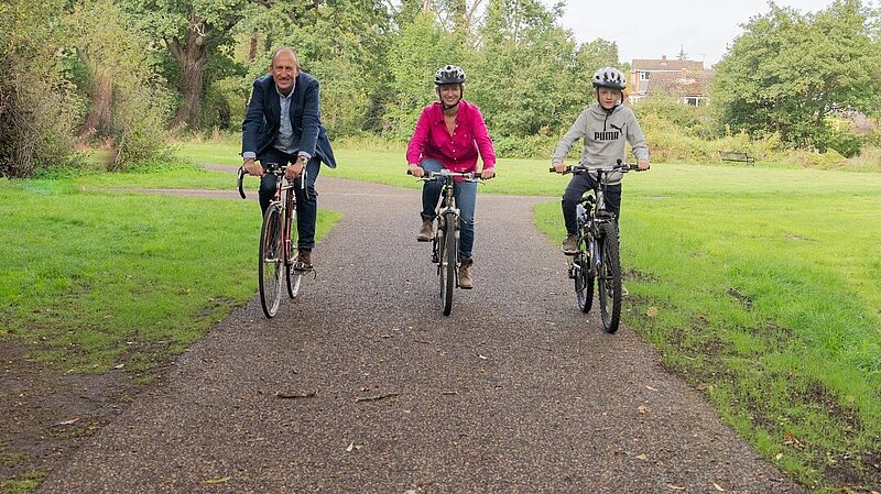 two adults and a teenager cycling on a cycle path in a field