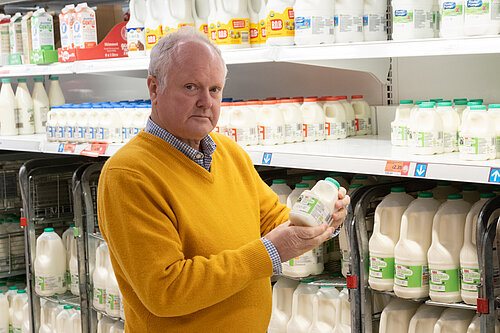 Clive Jones in the milk aisle of a supermarket, looking unimpressed at the price of a pint of milk.