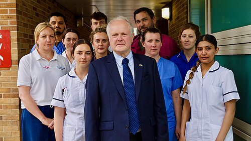 Clive Jones stood with NHS medical staff, looking serious.