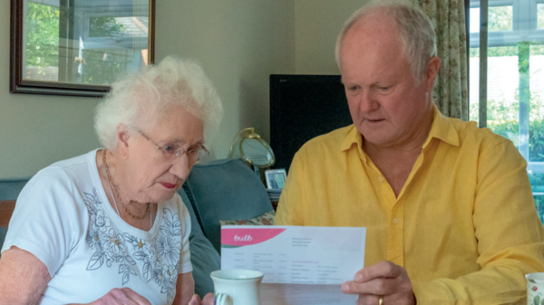 Clive Jones sitting down with an elderly lady in her home looking through the bills