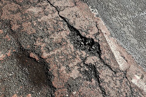 A couple of pot holes in on a damaged road surface